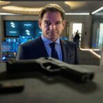 Michael Weatherly as Tony DiNozzo in a suit, looking directly forward with a serious expression, with a handgun in the foreground, from NCIS: Tony & Ziva Season 1 Episode 1 - No Country is Safe