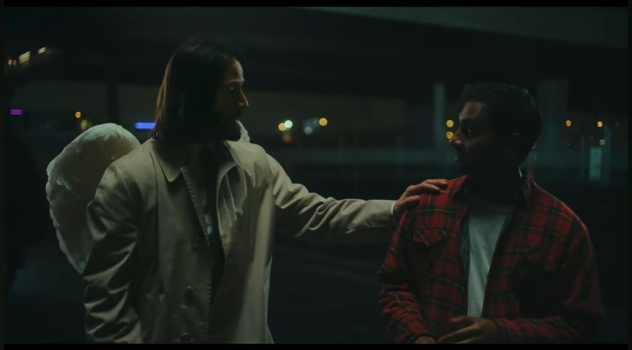 Keanu Reeves as an angel (Gabriel) with wings, putting a hand on Aziz Ansari's (Arch) shoulder in a night scene.