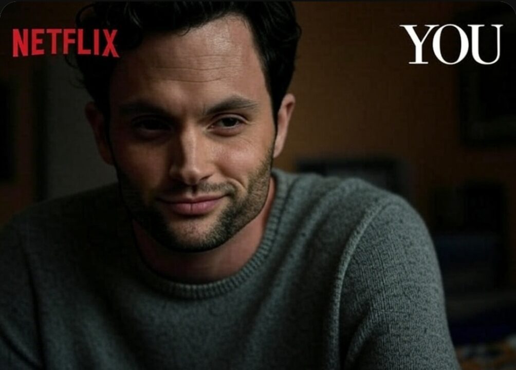 The image is a promotional shot likely for the Netflix series "YOU." It features a close-up of a man with dark hair and light skin, who appears to be actor Penn Badgley. He is wearing a gray sweater and looking directly at the camera with a subtle, somewhat knowing smirk on his face. His eyes are slightly narrowed, which could suggest a sense of calculation or hidden intent. The "NETFLIX" logo is visible in red in the upper left corner, and the white text "YOU" is positioned in the upper right corner. The background is softly blurred and appears to be an indoor setting with warm, muted tones. The overall lighting is soft and slightly dramatic, focusing attention on the man's expression.