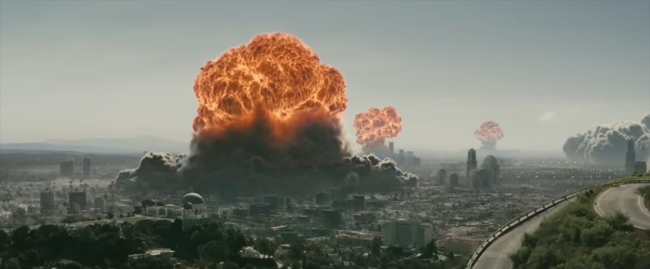 Multiple nuclear explosions engulf a sprawling cityscape under a hazy sky.