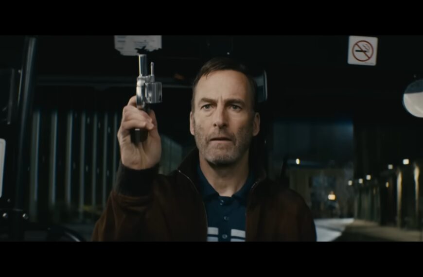 Bob Odenkirk as Hutch Mansell holding a small handgun on a public bus, confronting a group of assailants in a pivotal fight scene from the movie Nobody.