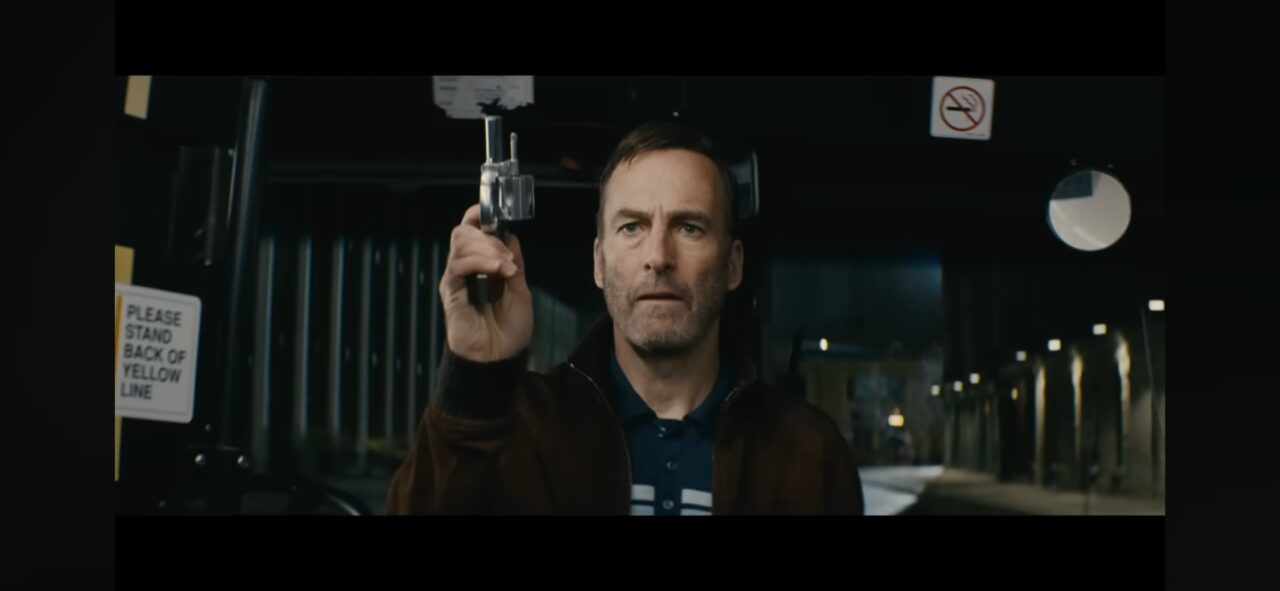 Bob Odenkirk as Hutch Mansell holding a small handgun on a public bus, confronting a group of assailants in a pivotal fight scene from the movie Nobody.