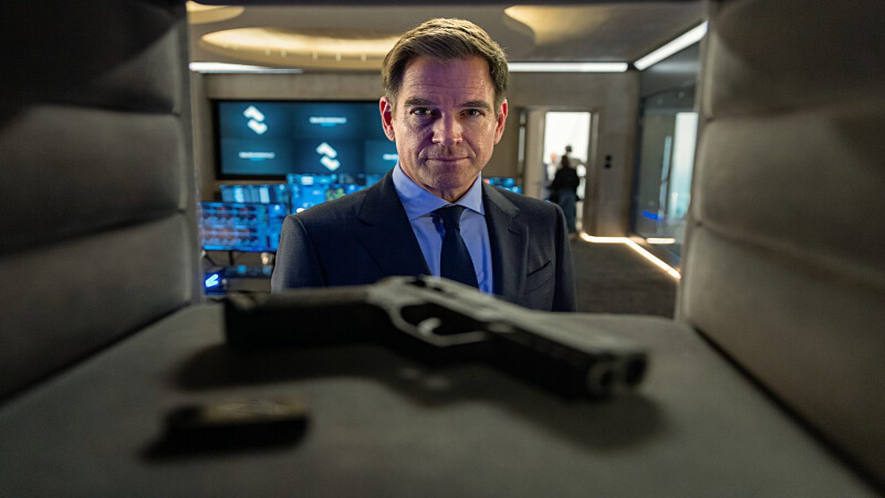 Michael Weatherly as Tony DiNozzo in a suit, looking directly forward with a serious expression, with a handgun in the foreground, from NCIS: Tony & Ziva Season 1 Episode 1 - No Country is Safe
