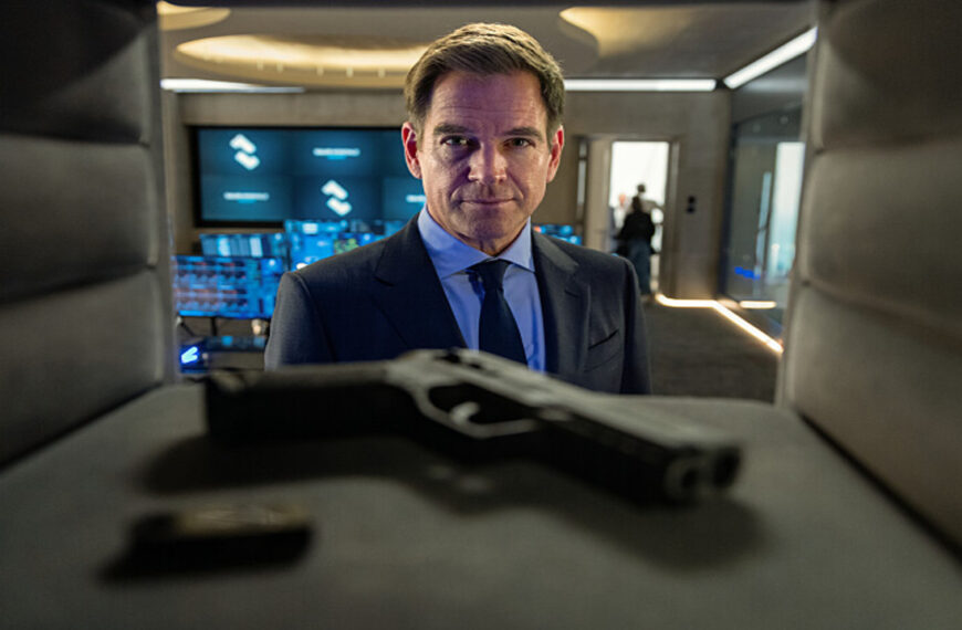 Michael Weatherly as Tony DiNozzo in a suit, looking directly forward with a serious expression, with a handgun in the foreground, from NCIS: Tony & Ziva Season 1 Episode 1 - No Country is Safe