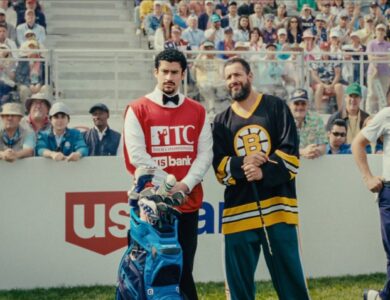 Adam Sandler as Happy Gilmore in his Boston Bruins hockey jersey, holding a golf club, standing next to his caddy on a golf course with spectators in the background.