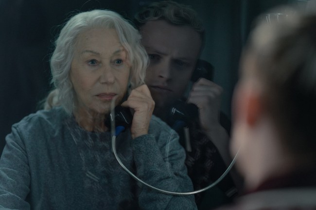 Maeve (played by Helen Mirren) on a prison phone call, looking serious, with a blurred young man in the background, conveying the manipulative and unsettling tone of the MobLand finale.