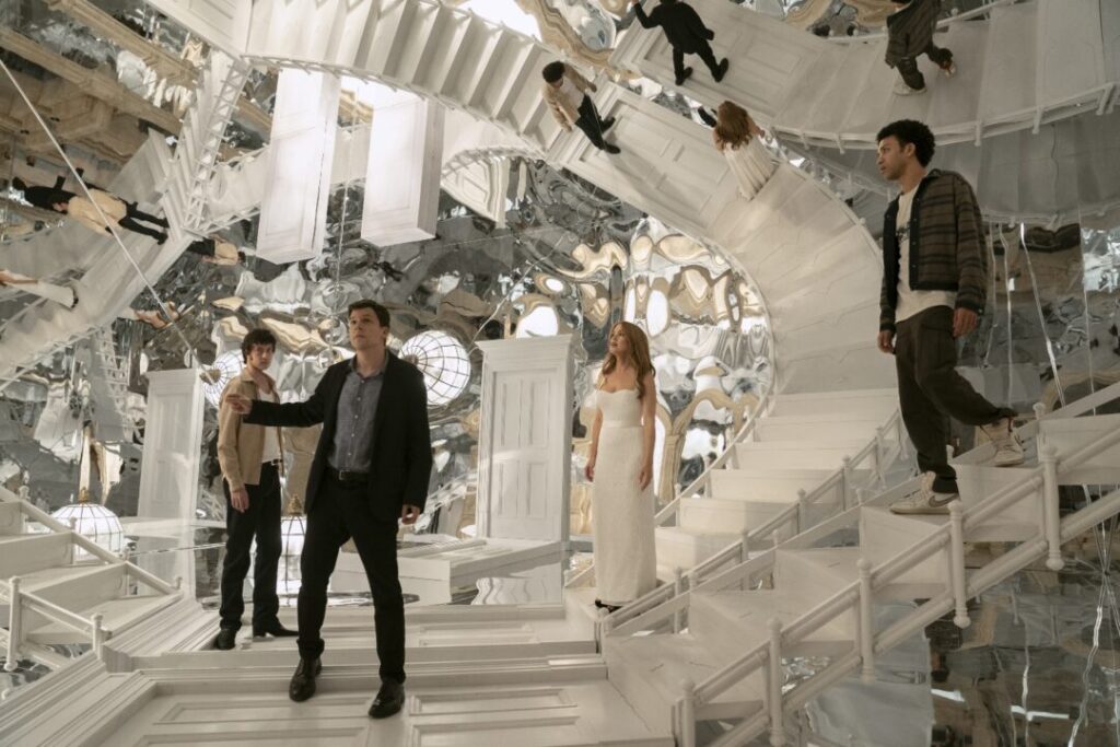 J. Daniel Atlas (Jesse Eisenberg) and Henley Reeves (Isla Fisher) navigating a visually complex room made of mirrors and white stairs in Now You See Me, Now You Don't, with other figures reflected.