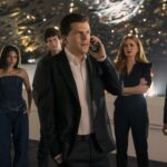 J. Daniel Atlas (Jesse Eisenberg) on a phone, surrounded by several other cast members, including Isla Fisher as Henley, and others, in what appears to be a large, modern, possibly event space, in Now You See Me, Now You Don't.