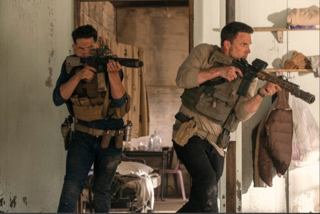 Ben Affleck as Christian Wolff and Jon Bernthal as Braxton, heavily armed and engaged in a gunfight inside a dilapidated building during The Accountant 2.