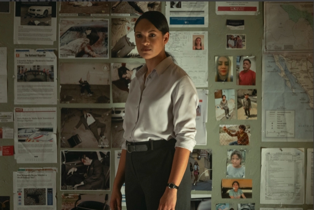 Marybeth Medina (Cynthia Addai-Robinson) stands in front of a wall covered with various crime scene photos, notes, and a map, looking contemplative.
