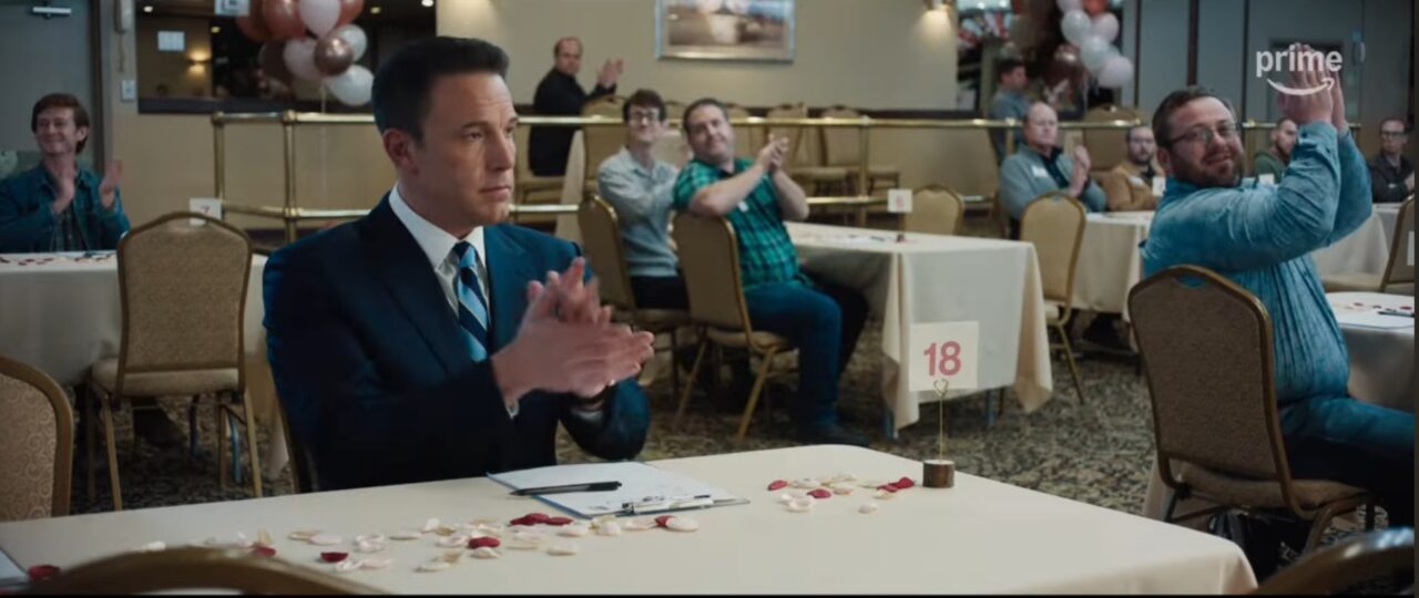Christian Wolff (Ben Affleck) awkwardly clapping at what appears to be a dating event in The Accountant 2, surrounded by other attendees.