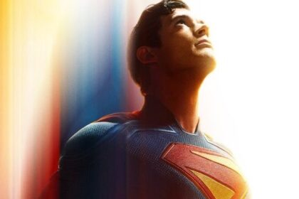 Superman, in his iconic blue and red suit with the S-shield, looks up intensely against a backdrop of glowing red, orange, and blue light streaks, conveying motion and power.