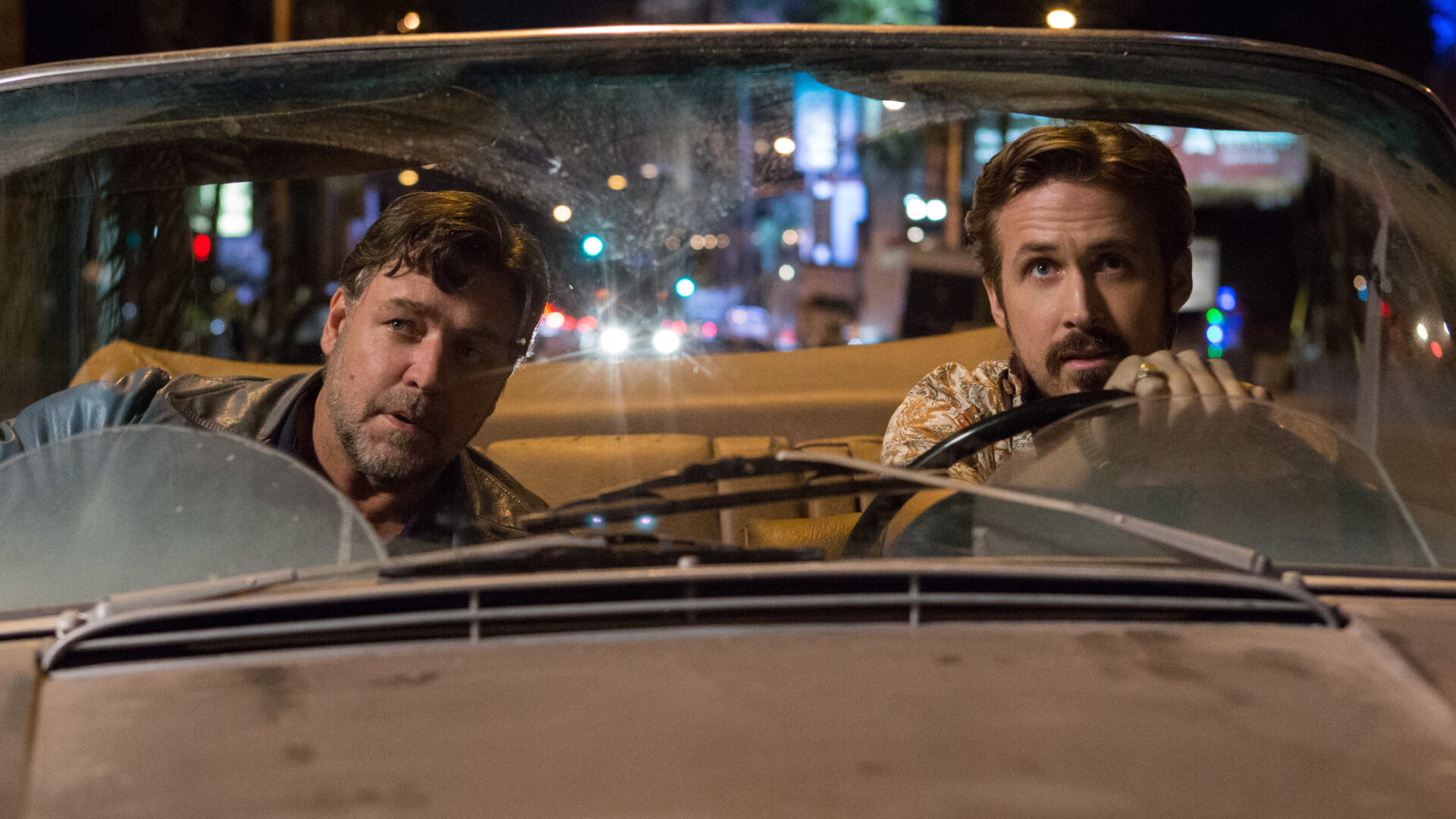 Russell Crowe and Ryan Gosling in a car at night, looking forward, with the Cinesist logo visible in the bottom right corner.